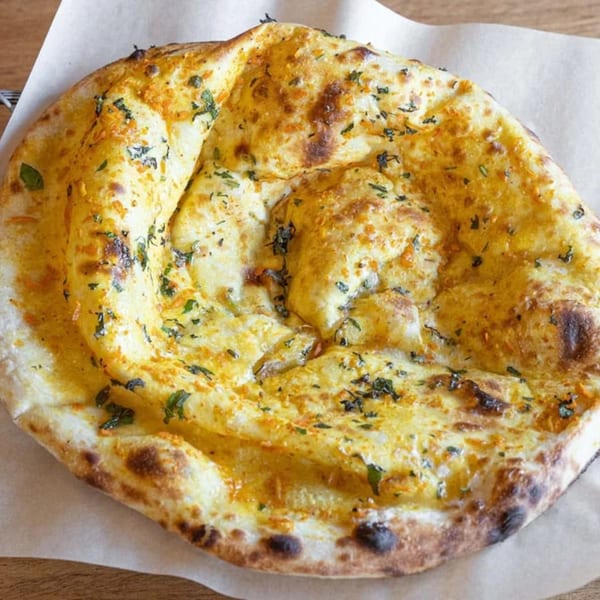 Golden brown naan bread, sprinkled with green herbs and spices, on a piece of parchment paper.