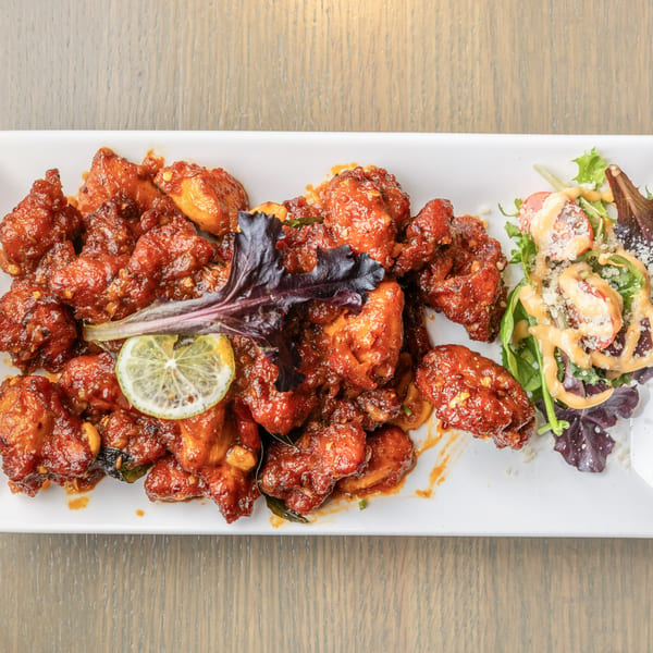 Spicy red chicken pieces with a lime slice and a side salad on a white rectangular plate.