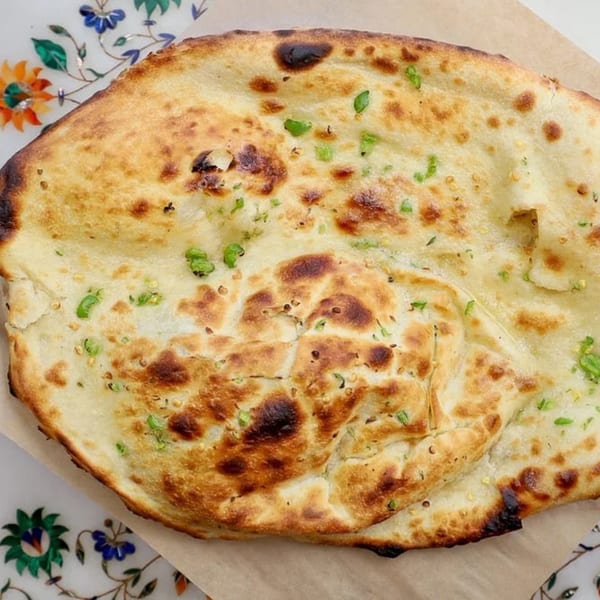 Golden brown naan bread, speckled with green herbs, rests on parchment paper and a decorative plate.